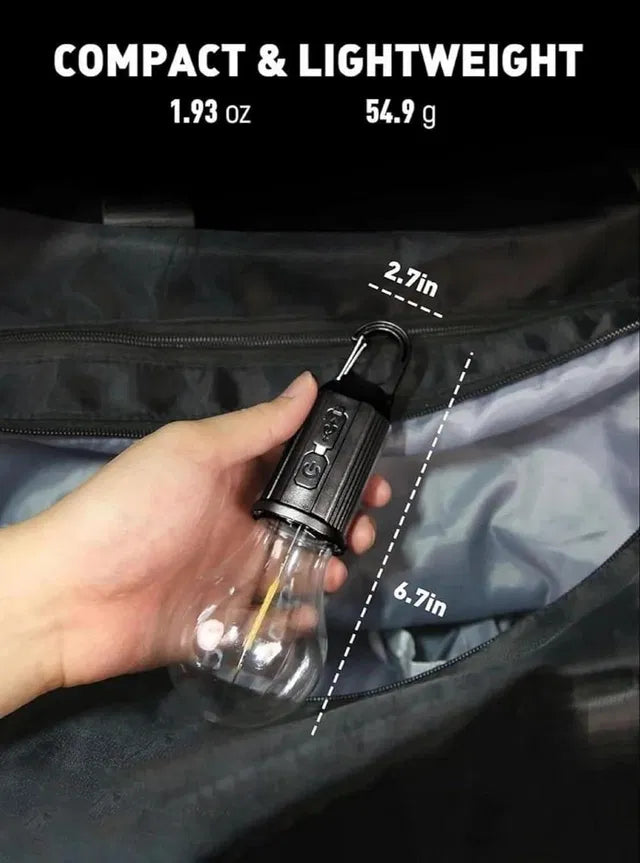 A hand holds the Decorative Hanging Bulb with 3 Modes Tent Lamp for Camping (Pack of 2), a compact LED lamp with carabiner, measuring 6.7"L x 2.7"W and weighing only 1.93 oz (54.9g). The tent lamp is displayed above a zippered bag.